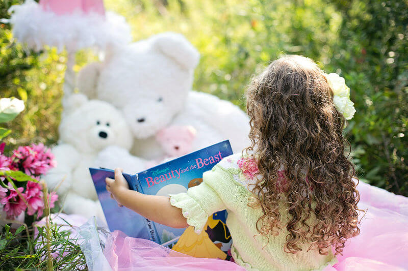 Little girl reading a book to her teddy bears in the woods